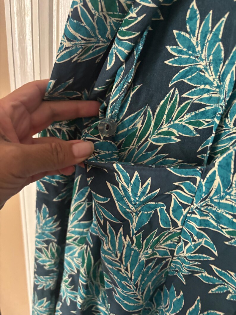 Puede incluir: Un vestido de estampado floral azul y verde con cierre de bot&oacute;n. El vestido tiene un bolsillo en el lado izquierdo.