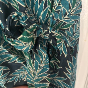 Puede incluir: Un vestido de envoltura con estampado azul y verde con un lazo en la cintura.