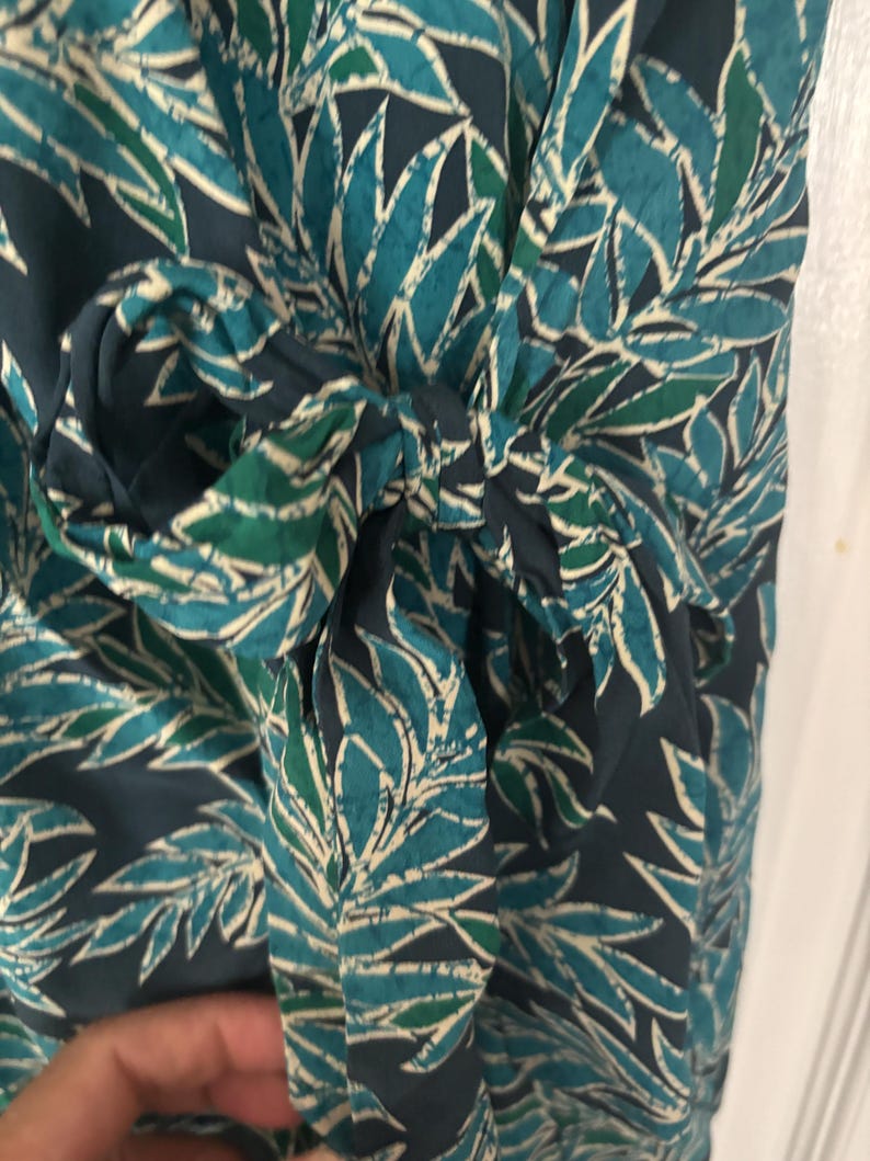 Puede incluir: Un vestido de envoltura con estampado azul y verde con un lazo en la cintura.