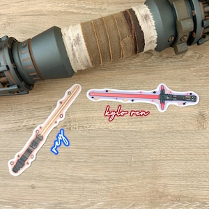 May include: Two Star Wars lightsaber stickers, one with a yellow blade and the text "Rey" and the other with a red blade and the text "Kylo Ren".