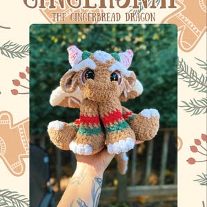 May include: A crocheted dragon plush toy with the text "Gingersnap The Gingerbread Dragon." The dragon is brown with white, red, and green details. It has large eyes and is designed to look like a gingerbread cookie.