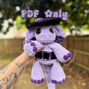 May include: Purple crocheted dragon wearing a black witch hat with a white band. The dragon has a black belt and purple feet. The text "PDF only" is written in pink letters above the dragon.
