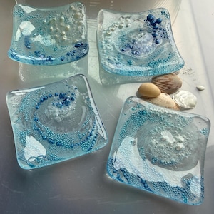 May include: A white ceramic mug with a black handle and the text "But First, Coffee" in a black, handwritten font. The mug is on a white surface.