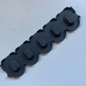 May include: A black rubber strip with six oval-shaped holes. The strip has a wavy edge and the text "FRS 10" is printed on the top.