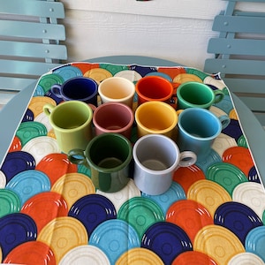 May include: A set of ten colorful mugs with a variety of colors including green, blue, yellow, red, and brown. The mugs are arranged in a circle on a colorful table runner with a pattern of overlapping circles.