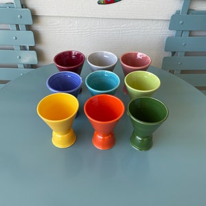May include: A set of ten colorful ceramic cups, each with a different color and a unique design. The cups are arranged in a circle on a blue table.