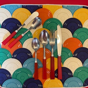 May include: Set of five red handled silverware pieces on a colorful patterned placemat. The set includes a butter knife, two spoons, a fork, and a dinner knife.