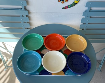 Może przedstawiać: Zestaw kolorowych ceramicznych misek w metalowej tacy na niebieskim stole. Miski są w różnych kolorach, w tym zielonym, pomarańczowym, żółtym, niebieskim i białym. Dekoracyjna jaszczurka jest zamontowana na ścianie w tle.