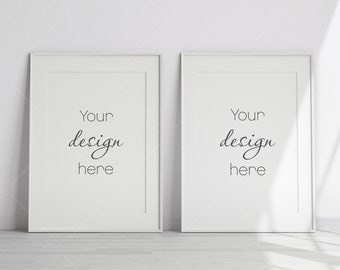 May include: Two white picture frames with a white background. The frames are hanging on a white wall. The text "Your design here" is written in black inside each frame.