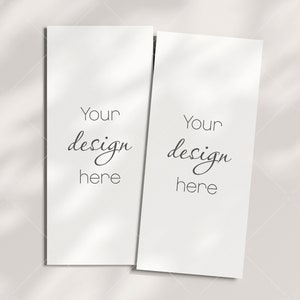 May include: Two blank white cards with the text "Your design here" on each card. The cards are on a white surface with shadows from a window.