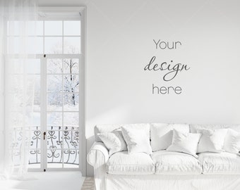 May include: A white couch with white pillows in a white room with a window overlooking a snowy scene. The text "Your design here" is written on the wall.