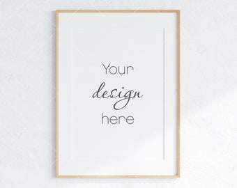 May include: A simple, white frame with a light wood border. The frame is hanging on a white wall and has the text "Your design here" written in black.