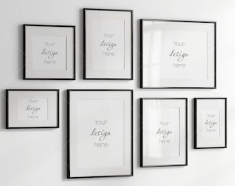May include: A set of seven black picture frames of various sizes, arranged on a white wall. Each frame has a white mat and the text "Your design here" is written in black cursive inside each frame.