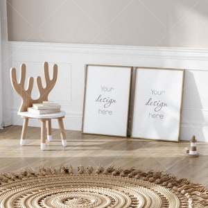 Op de afbeelding: Twee gouden gelijstte posters met de tekst "Your design here" op een witte achtergrond. De posters hangen aan een witte muur boven een bruine houten vloer. Een houten hertenstoel met een witte zitting en een bruin geweven tapijt bevinden zich op de voorgrond.