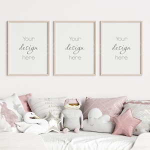 Puede incluir: Tres marcos de madera con el texto "Your design here" colgados en una pared blanca sobre una cama blanca con almohadas rosas y blancas.