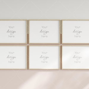 May include: Six empty picture frames with a light wood finish are arranged in a grid pattern on a light pink wall. The frames are all the same size and have a simple, modern design. The text "Your design here" is written in each frame.