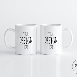 Peut inclure: Deux tasses en céramique blanche avec du texte noir qui dit "YOUR DESIGN HERE" sur chaque tasse. Les tasses sont sur une surface blanche.