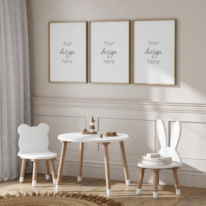 Puede incluir: Un juego de mesa y sillas de madera blanca para niños. La mesa tiene una tapa redonda y cuatro patas. Las sillas tienen un asiento y un respaldo de madera blanca con respaldos en forma de conejo y oso. Las sillas tienen patas pintadas de blanco. Hay tres cuadros dorados en la pared detrás de la mesa. Los cuadros tienen el texto "Your design here".