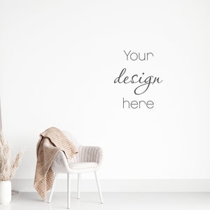 Może przedstawiać: Białe krzesło z beżowym kocem zarzuconym na oparcie, wazon z suszoną trawą pampasową i szary zasłoną w tle. Ściana jest biała z napisem "Your design here" napisanym czarnym kolorem.