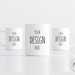 May include: Three white ceramic mugs with black text that reads "Your Design Here" on each mug. The mugs are arranged in a row on a white surface.