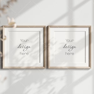 Op de afbeelding: Twee vierkante houten fotolijsten met een lichtbruine afwerking, hangend aan een witte muur. De lijsten zijn leeg en hebben de tekst "Your design here" in zwarte cursieve letters in elk lijst.