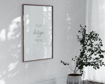 May include: A brown wooden frame with a white mat and a white background. The frame is hanging on a white wall. The text "Your design here" is visible in the frame. A potted plant with green leaves is in the corner of the room.