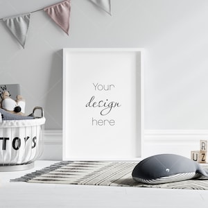 May include: A white framed picture with the text "Your design here" hanging on a white wall. A white basket with the word "TOYS" on it is filled with stuffed animals. A black and white striped whale plush toy is on a black and white rug. Wooden blocks with letters on them are scattered on the floor.