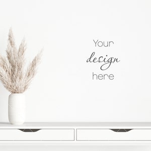 Może przedstawiać: Biały, żebrowany ceramiczny wazon z suszoną trawą pampasową, ustawiony na białym stole konsolowym z dwiema szufladami. Słowa "Your design here" są napisane czcionką skryptową na białej ścianie.