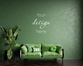 May include: A green velvet sofa with three pillows and a green round pillow sits in front of a green wall. The text "Your design here" is written on the wall. A large green plant in a black pot is on the left side of the image.
