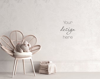 Puede incluir: Una silla de mimbre blanca con un respaldo en forma de flor y un conejito de crochet sentado en el asiento. La silla está frente a una pared blanca con el texto "Your design here" escrito en ella. Hay una pila de mantas de punto blancas en el suelo junto a la silla.