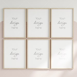 Op de afbeelding: Zes vierkante frames met een lichte houtkleurige afwerking zijn in een rasterpatroon op een lichtroze muur gerangschikt. Elk frame heeft een witte passe-partout en een witte achtergrond met de tekst "Your design here" in zwarte cursieve letters.