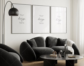 May include: Three black framed posters with the text "Your design here" hanging on a white wall above a black sofa with three pillows. A black floor lamp with a round black shade is in the corner of the room. A black coffee table with a black marble top is in front of the sofa.