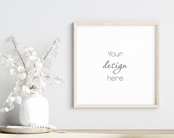May include: A square, light wood-framed picture frame with the text "Your design here" on a white background. A white vase with white foliage sits to the left. A wooden tray with white beads is in front of the vase.
