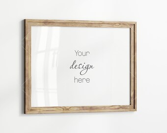 May include: A rectangular wooden picture frame with a light brown finish. The frame has a white interior with the words "Your design here" in black script. The frame is hanging on a white wall.