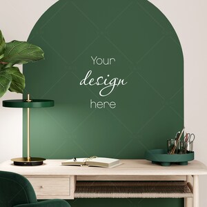 May include: A green desk lamp with a gold base sits on a light wood desk with a green chair. A green tray with writing utensils sits on the desk. The wall behind the desk is painted green and has the text "Your design here" written on it.