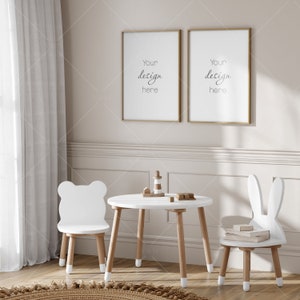 Puede incluir: Un juego de mesa y sillas de madera blanca para niños. La mesa es redonda y tiene cuatro patas. Las sillas tienen respaldos con forma de animales, una es un oso y la otra un conejo. Las sillas tienen asientos blancos y patas de madera. Hay dos carteles enmarcados en la pared detrás de la mesa, cada uno con el texto "Your design here".