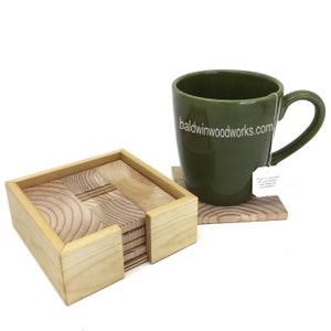 May include: A set of wooden coasters with a matching holder, alongside a green mug. The coasters have a natural wood grain design. The mug has the text "baldwinwoodworks.com" printed on it.