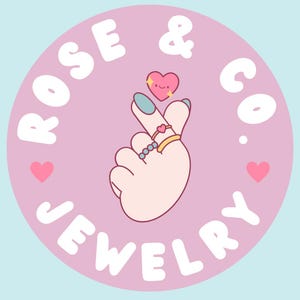 May include: A logo for Rose & Co. Jewelry, featuring a light pink circle with the text "ROSE & CO. JEWELRY" in white. A hand with rings makes a heart shape, with a smiling heart above. Two pink hearts are on either side.