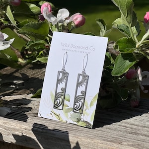May include: Silver earrings with a sun and wave design. The earrings are on a white card with the text "Wild Dogwood Co. Handcrafted Jewelry".