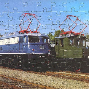 Puede incluir: Dos locomotoras eléctricas en vías de tren. La locomotora de la izquierda es azul y tiene el número "114-343" en el lateral. La locomotora de la derecha es verde y tiene el número "1012" en el lateral.