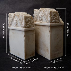 Puede incluir: Dos sujetalibros rectangulares de piedra color hueso con remates en front&oacute;n que presentan relieves de rostros humanos y motivos florales. El m&aacute;s peque&ntilde;o mide 13,5 cm de alto, 8,5 cm de ancho y 4 cm de fondo, pesando 1 kg. El m&aacute;s grande mide 15 cm de alto, 5,5 cm de fondo, pesando 1,5 kg.