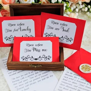Peut inclure: Une boîte en bois avec trois cartes rouges portant les inscriptions « Open when You feel Lonely », « Open when You are Sad » et « Open when You Miss me ». Une enveloppe rouge avec un sceau de cire est également présente.