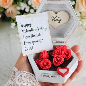May include: A white wooden hexagonal box with a hinged lid. The box is open and contains a small bouquet of red felt roses. A white card with the text "Happy Valentine's Day Sweetheart! Love you for Ever!" is visible in the box. A wooden heart with the name "Katy" is visible on the lid of the box.
