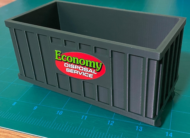 K&ouml;nnte beinhalten: Ein dunkelgr&uuml;ner Plastikcontainer mit einem roten ovalen Aufkleber, auf dem "Economy Disposal Service" in gr&uuml;nen Buchstaben steht.