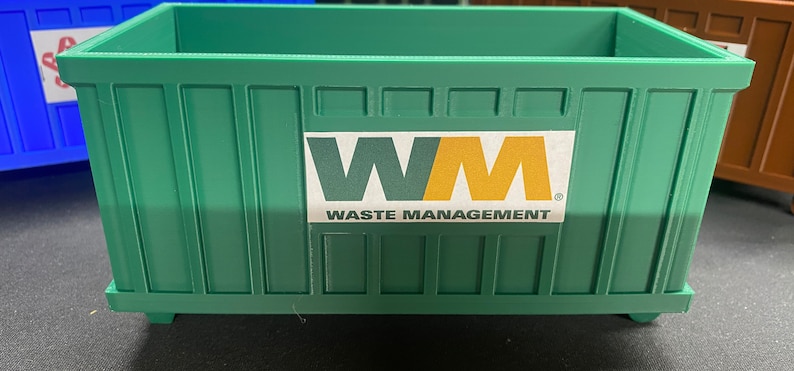 K&ouml;nnte beinhalten: Ein gr&uuml;ner Metallcontainer mit einem wei&szlig;en Etikett mit der Aufschrift "WM WASTE MANAGEMENT".