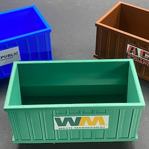 K&ouml;nnte beinhalten: Drei Miniatur-Abfallcontainer aus Plastik, einer blau mit "REPUBLIC SERVICES" aufgedruckt, einer braun mit "ACE RECYCLING & DISPOSAL" aufgedruckt und einer gr&uuml;n mit "WM WASTE MANAGEMENT" aufgedruckt.
