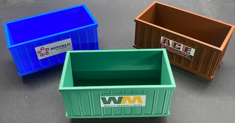 K&ouml;nnte beinhalten: Drei Miniatur-Abfallcontainer aus Plastik, einer blau mit "REPUBLIC SERVICES" aufgedruckt, einer braun mit "ACE RECYCLING & DISPOSAL" aufgedruckt und einer gr&uuml;n mit "WM WASTE MANAGEMENT" aufgedruckt.