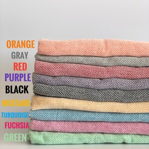 Peut inclure: Une pile de dix serviettes en tissu de différentes couleurs, dont orange, gris, rouge, violet, noir, moutarde, turquoise, fuchsia et vert.