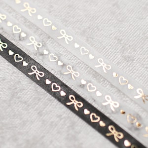 May include: Three rolls of washi tape with gold foil hearts and bows on a white background. The tape is black and white.