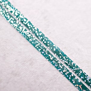 May include: Two strips of teal washi tape with white glitter accents on a white background.